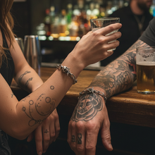 Load image into Gallery viewer, Two people with tattoos holding hands in a bar setting